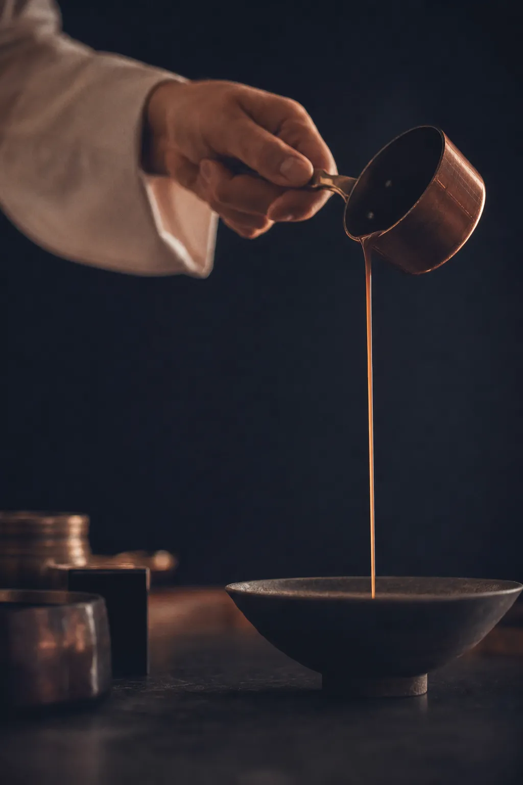 Hand eines Kochs gießt Sauce aus einem kleinen Kupfertopf